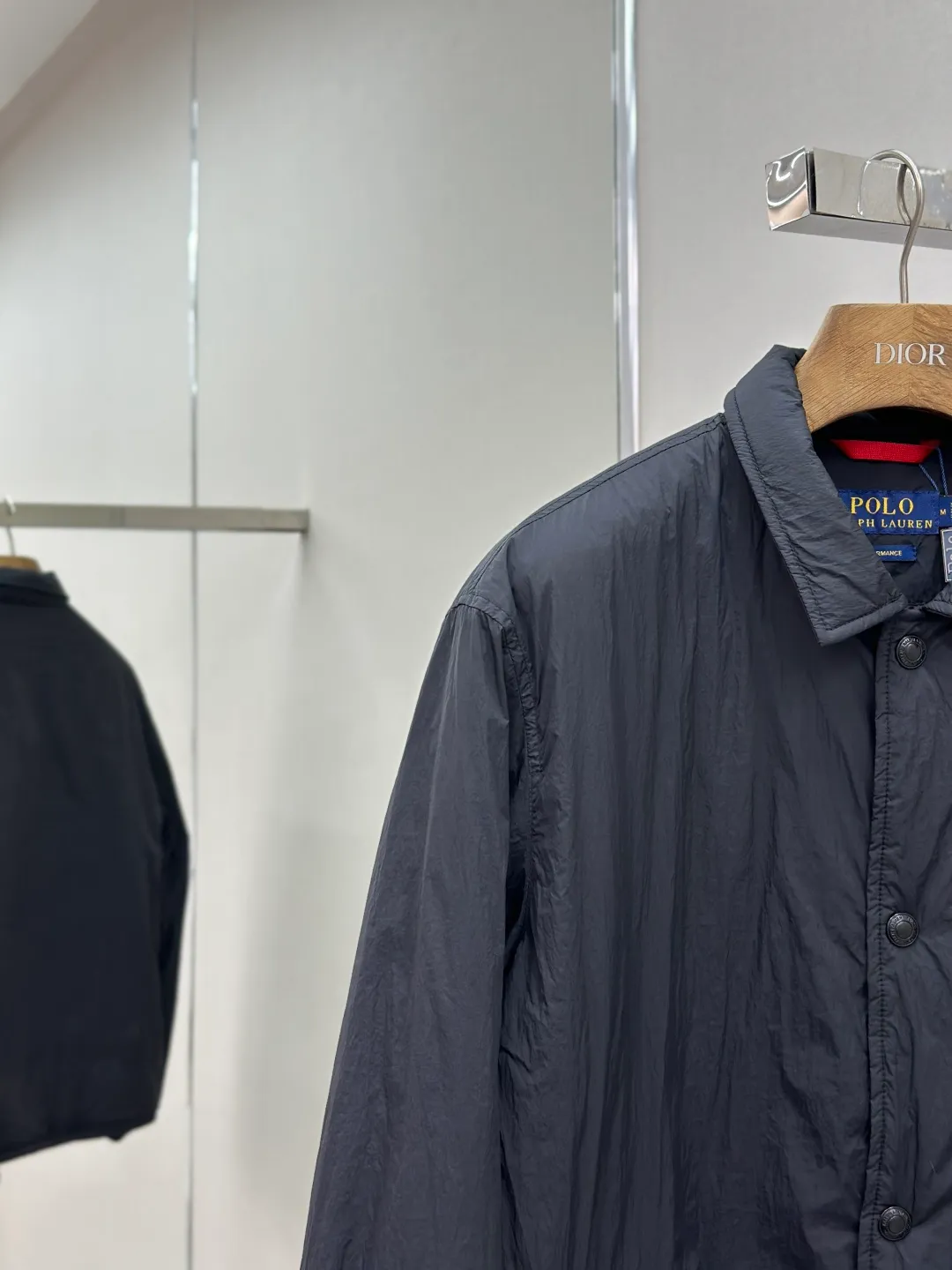 P650 RAH LAUREN RL red label lapel is light and thin. It is made of high-density nylon taffeta with a density of about 210T-300T. The surface is smooth and slightly matte. It has excellent windproof and waterproof performance (with R water-repellent treatment). It has strong wrinkle resistance and is easy to care for. It adopts the vat dyeing process (the dye penetrates into the fiber) and the color fastness reaches ISO level 4 or above to avoid fading or color transfer after washing. The lightweight cotton-polyester blend lining (65% Polyester + 35% Cotton) reduces the friction between the fabric and inner clothing and improves the smoothness of wearing. The blended material combines breathability and durability to avoid the stuffy feeling of pure nylon lining. The classic coach (Jaet) loose fit has a slightly dropped shoulder line (the shoulder width is 1-2cm wider than the standard fit), the length reaches the hips, and the sleeves are slightly tapered straight sleeves, taking into account freedom of movement and casual style. Flat satin stitch embroidery (satin embroidery), using 100% polyester high color fastness embroidery thread (the color number is consistent with the brand's standard red color card), the stitch density is 12-15 stitches cm, the outline of the horse logo is clear, and the details of the rider and horse are burr-free. Precise positioning through the template (12cm from the bottom of the collar and 8cm from the placket) ensures symmetry and centering. The seams of the body are made of double-needle flat seams (needle pitch 3cm, 10 needles), the stitches are flat and straight, the stitching color is dark black (the same color as the fabric), and the stitch width is 0.5cm, which enhances firmness and forms simple decorative lines. The placket is made of double-layer folding + flat seam splicing, with a thickness of about 0.3cm to ensure that the buttons are not easily deformed when fixed; the edges of the placket are cut with a hot knife to avoid burrs. The armholes are machine stitched with round head keyholes and flat seams. After stitching, the armholes have a natural curvature and no sense of tightness during movement. The height of the sleeves is about 8-10cm, which is in line with the casual and loose characteristics. Black urea resin button with matte surface treatment. The buttonholes are hand-made keyholes (6 strands of cotton thread, keyhole density of 8 stitches mm), and the edges of the eyelets are smooth and without burrs. The first button on the neckline is a hidden button (diameter 12mm), which prevents the neckline from opening and improves the neatness of wearing. Size:S-XL